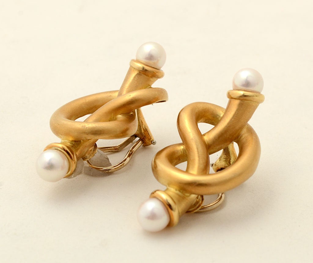 These are unusual eighteen karat gold pretzel shaped earrings with pearl tips by Angela Cummings. They have a matte finish with glossy bands around the pearls. Backs are clips to which posts can easily be added.