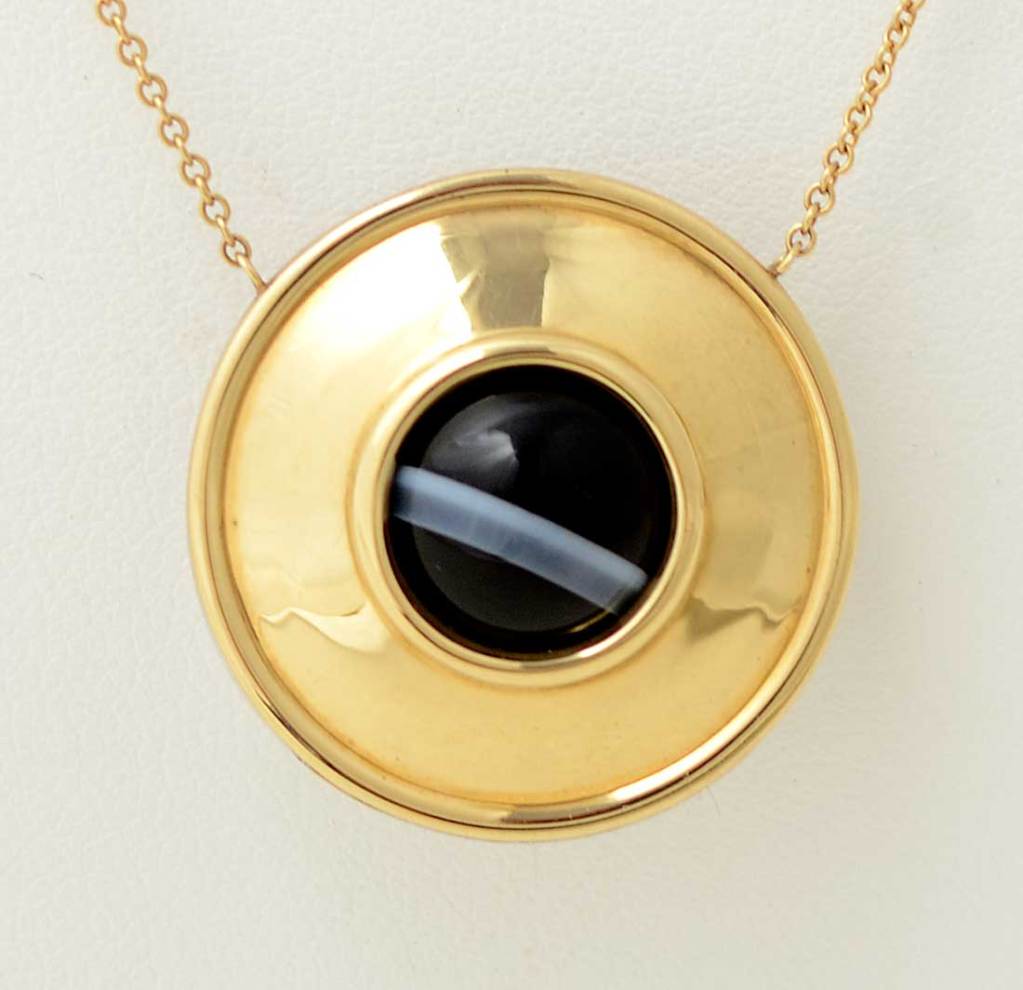 Reversible pendant necklace by Paloma Picasso for Tiffany. One side is eighteen karat gold and the other sterling silver. A banded agate stone revolves in the middle allowing the variations in the stone to show. It is strung on a gold chain also