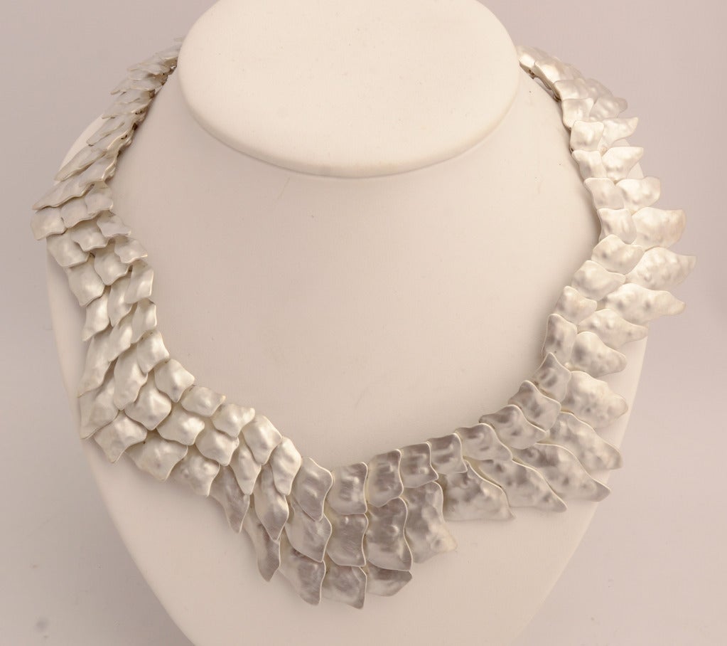 Wonderful asymmetrical necklace by Mexican architect turned jeweler, Eduardo Herrera. Herrera refers to this as his Crocodile Tail necklace.  Various size links overlap to create what one might see as a reptilian skin. Each link is hammered and