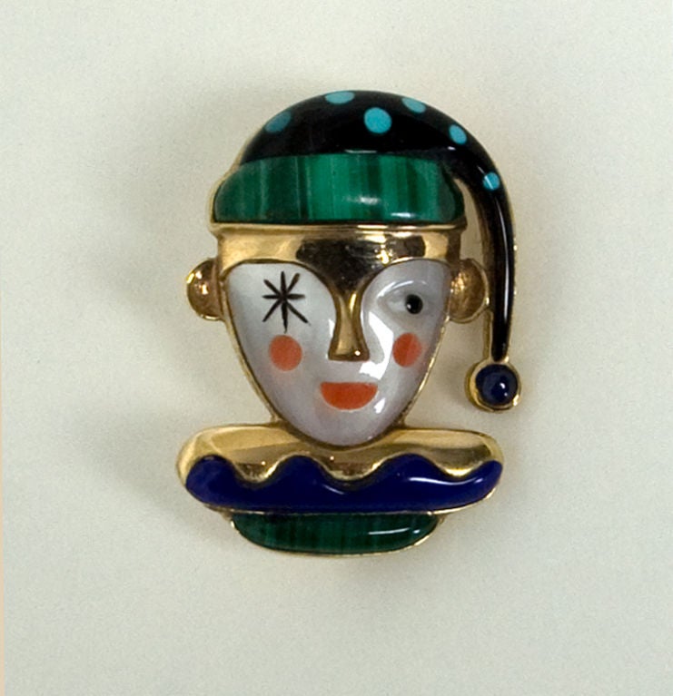 Winking jester pendant/ brooch skillfully combining a variety of stones. The face is mother of pearl with coral lips and cheeks. His cap is malachite and onyx with turquoise dots. The collar is lapis lazuli and malachite. All are set in 14 karat