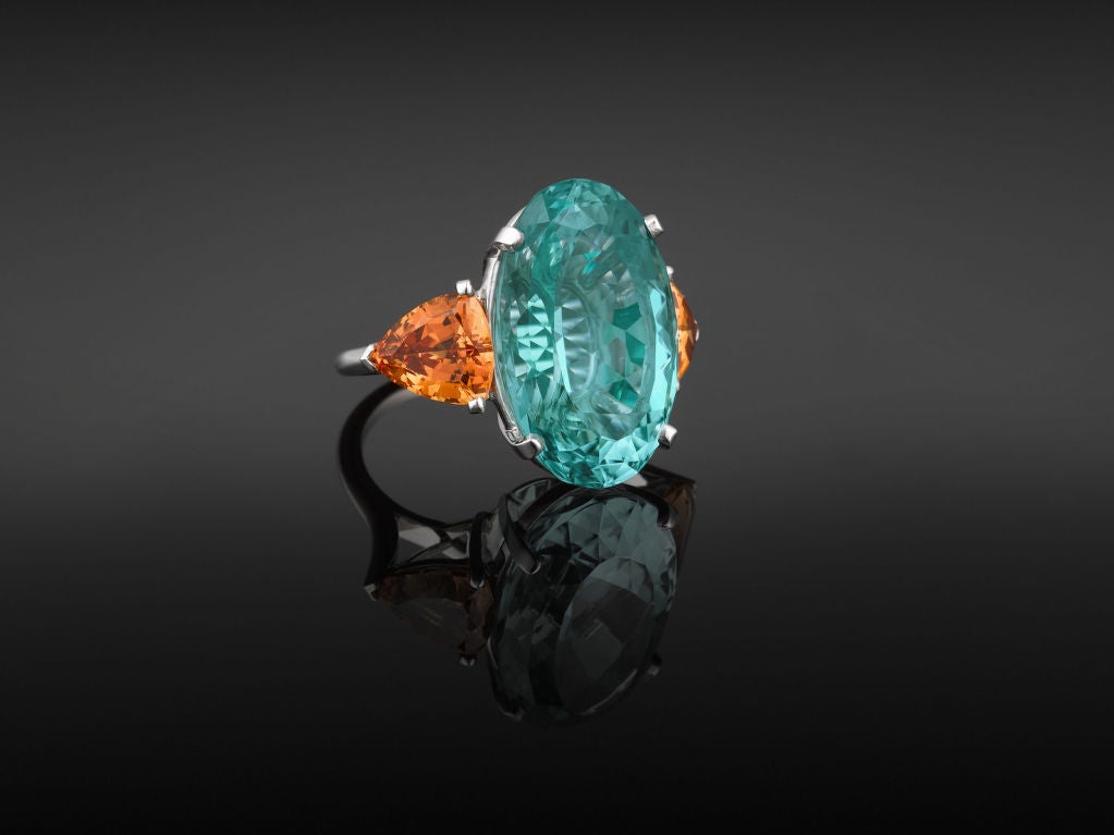 The fire and radiance of trillian-cut orange garnets and an amazing 22.81 carat oval-cut aqua-blue Paraiba tourmaline make a daring statement in this exquisite platinum ring. The garnets weigh approximately 5.38 carats, and provide just the perfect