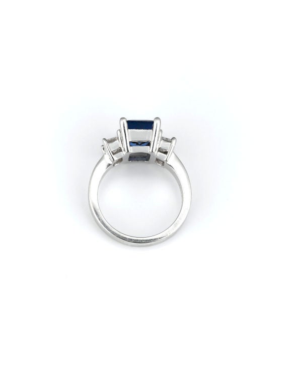 A stunning, royal blue emerald-cut sapphire weighing 3.08 carats is flanked by a pair of glistening white diamonds in this beautiful ring. The gems in this platinum ring are emerald cut, testifying to their superior clarity and overall quality.