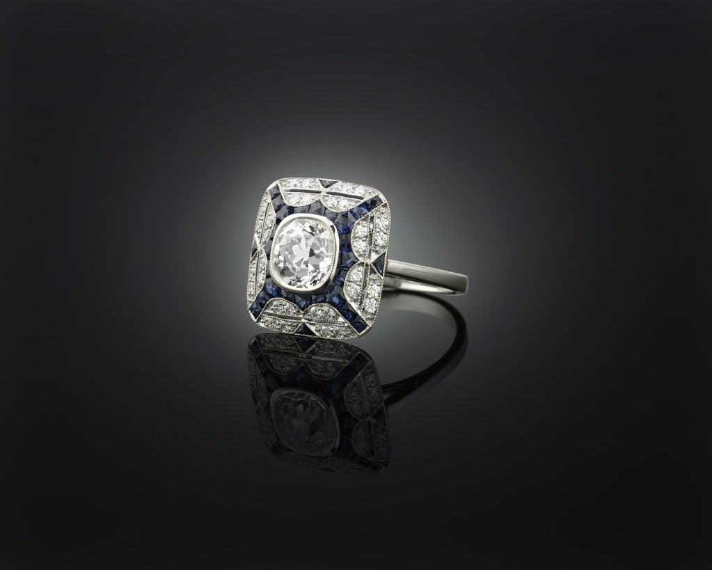 Geometric design and bold, contrasting color define this diamond and sapphire ring. A 1.22 carat diamond glistens in its center, surrounded by 1.84 carats of deep blue sapphires and .24 carats of additional diamonds. The sleek refinement that