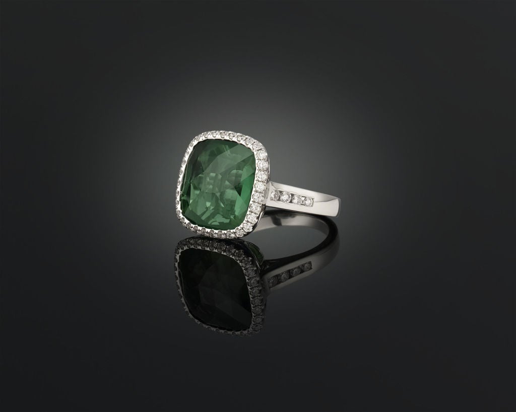 A captivating green tourmaline glows in this elegant ring. Weighing an outstanding 12.62 carats, the cushion-cut stone displays the deep blue-green hue found in the most desirable of these stones. Set amongst .76 carats of sparkling white diamonds