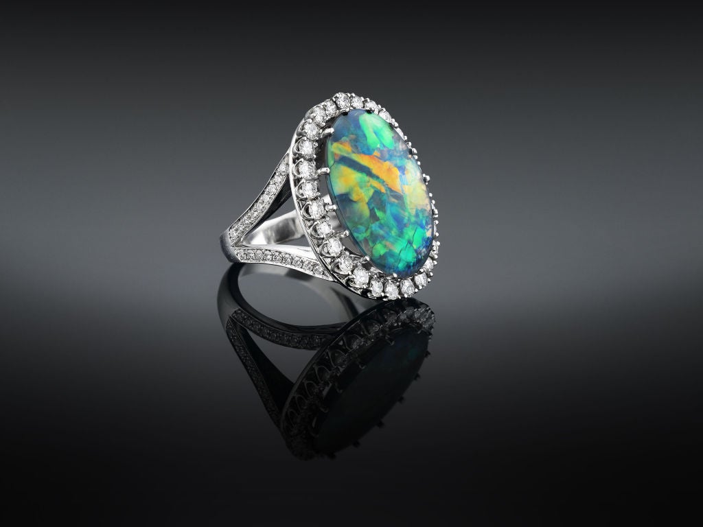 Dynamic beauty and exceptional color recommend the striking black opal in this eye-catching ring. Weighing 9.10 carats, this stunning gem exhibits fiery reds and oranges harmonizing with cool greens and blues, while 1.52 total carats of diamonds in