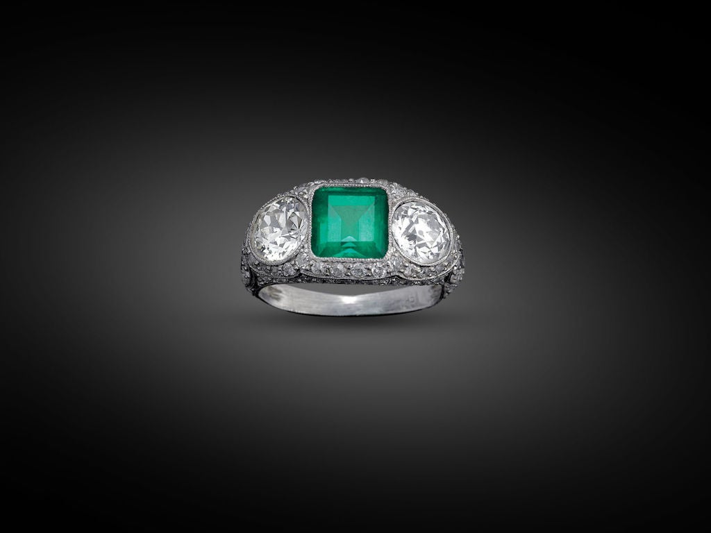 This striking emerald and diamond ring captures the timeless sophistication of the Art Deco style. Mounted in an ornate platinum dome setting, a magnificent emerald, weighing approximately 2.00 carats, is joined by two spectacular European cut