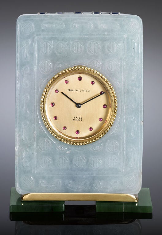 Crafted of two types of jade, this enchanting classic table clock by the renowned Van Cleef & Arpels is the epitome of elegance. Luminous carved jadeite frames the gold timepiece, which features 12 ruby cabochons marking each hour. Set upon feet of