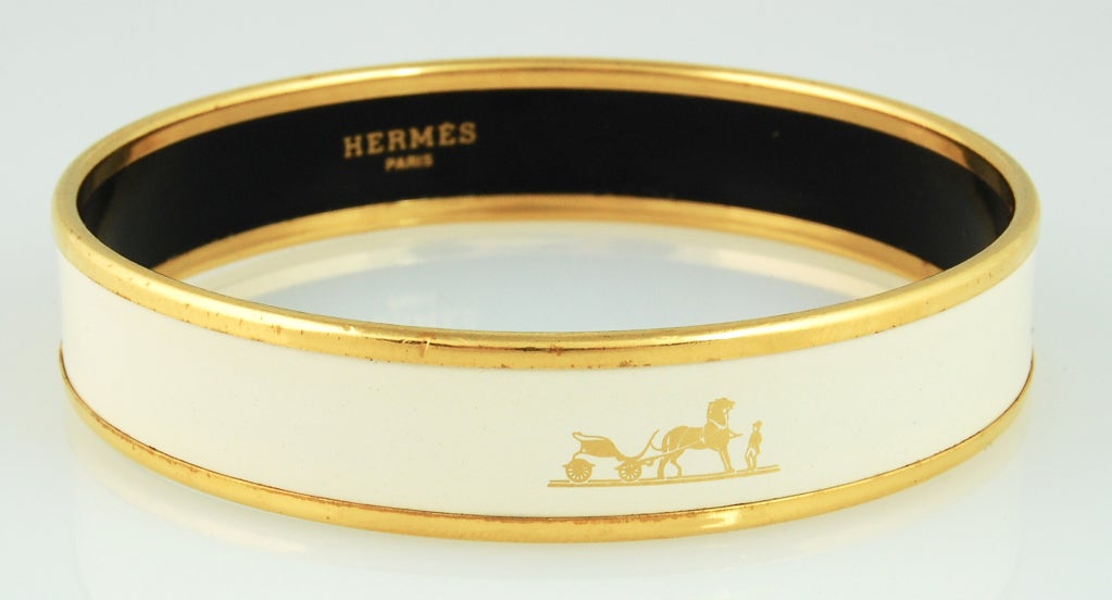 Hermes bangle with gold-plated rim and cream-colored band with gold printed horse drawn carriage. 

Interior reads HERMES Paris Made in Austria + L
