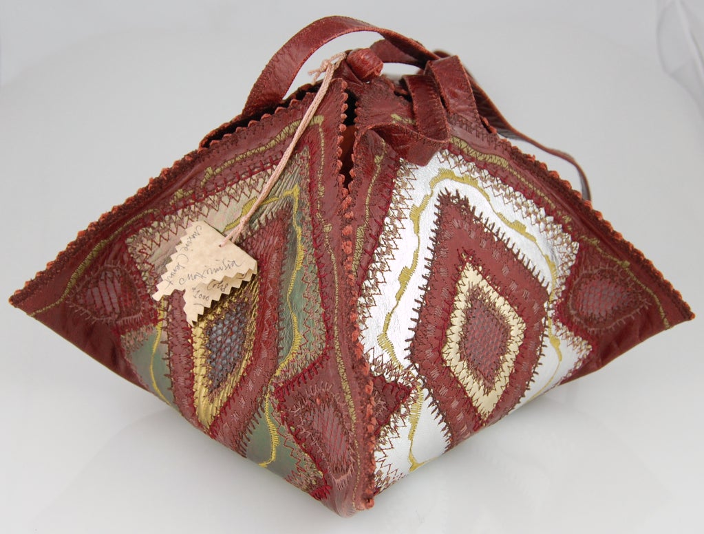 An intricate leather one-of-a-kind purse artisan-made in NYC during the 1970s. Wine red base with accents of gold and silver metallic leather, wine reptile skin, and yellow, green and wine decorative stitching. 

Maxine Clement made all her bags