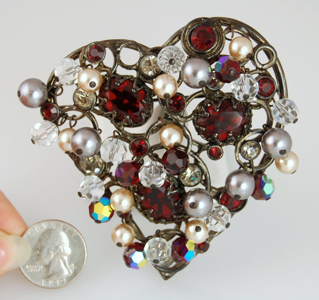 An impressive oversized heart-shaped metal brooch encrusted with red and clear crystal gems and dripping with clear and red faceted crystal beads and faux pearls.
Has appropriate hardware to be worn as a brooch or pendant. 
Signed YSL MADE IN
