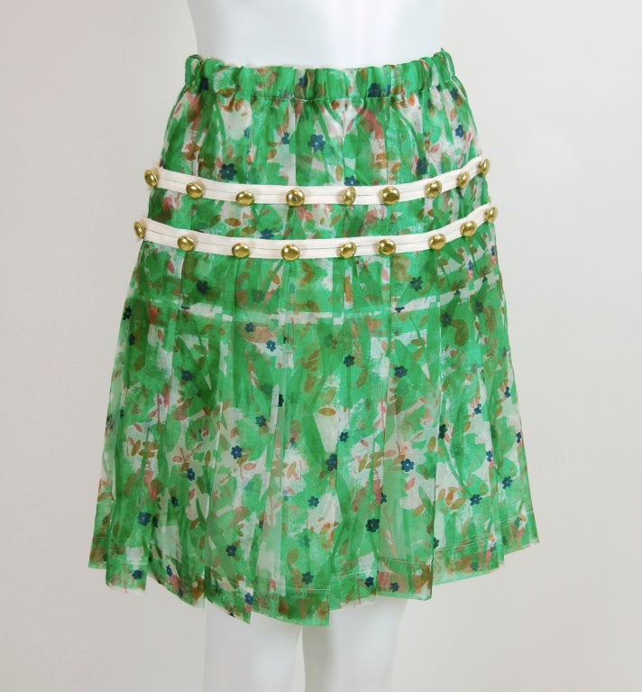 Printed sheer green, pink and navy pleated floral skirt with white cotton tape and brass button details. Pull-on style with elastic and drawstring waist. Unlined.

From the now-discontinued Comme des Garçons sub-label.

100% Polyester