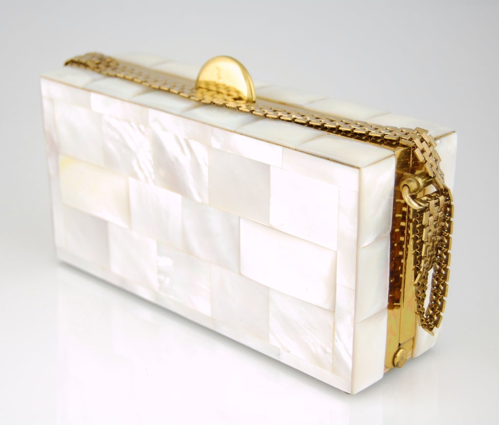 Here's a stunning art-deco inspired minaudière completely covered in mother-of-pearl tiles! Concentric arches clasp and metal mesh strap in plated brass. Interior is lined in racy red satin and has pockets for the matching compact and lipstick case