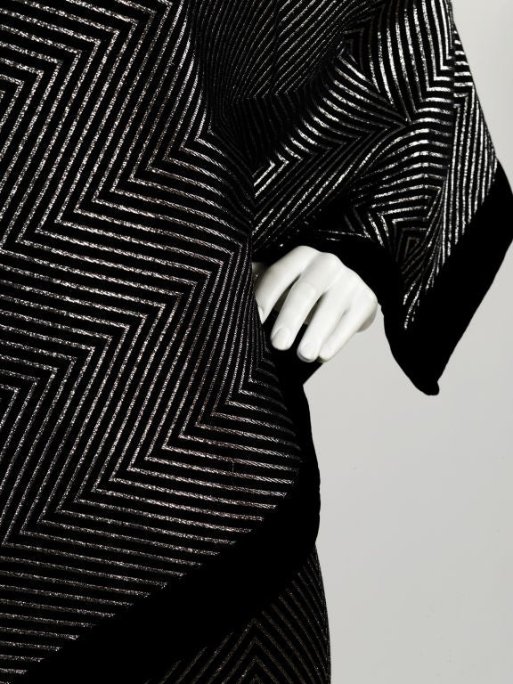 1970s Gucci one-shouldered black silk lamé shift dress with attached asymmetrical caplet. Silver metallic zig-zag weave and lush velvet trim.