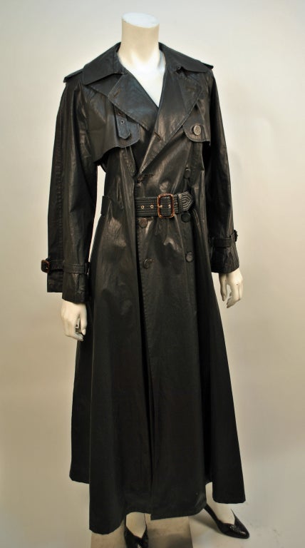 Jean Paul Gaultier's 'FEMME' black maxi length trench coat is made of a coated Polyurethane, which is great for waterproofing this stylish trench when battling the elements! With buckles and straps that run up the collar allowing it to be secured