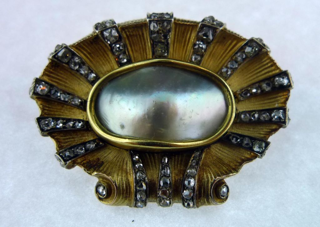 Elaborate blister pearl brooch is hand made to resemble a scallop shell.  The  bezel set center pearl is 23 X 13MM in size.  Old mine cut diamonds of varied size radiate from the center.  The surface of the gold work is ribbed.  Back of pin is