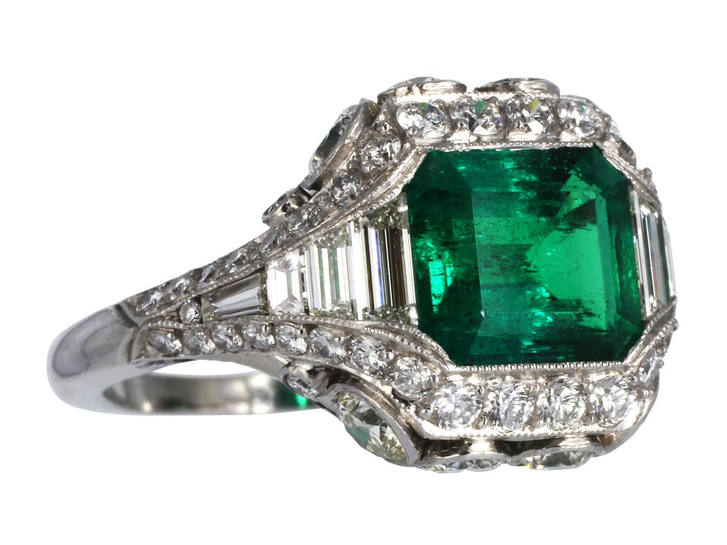 Platinum custom made Colombian Emerald and diamond filagree ring with millgrain edges. Consisting of one bezel set emerald cut Emerald weighing approximately 2.26 carats and calibre cut emeralds along the undergallery. The emeralds are accented with