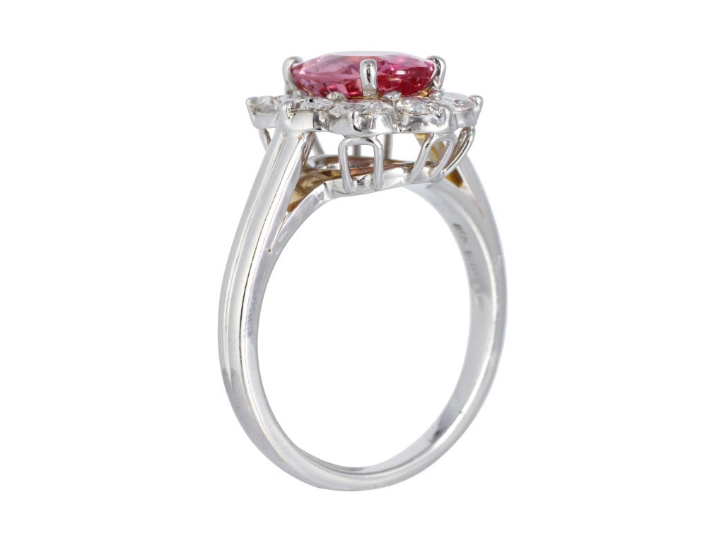 Platinum cluster ring consisting of 1 oval shaped Padparadscha sapphire weighing 2.43 carats, measuring 9.65 x 7.65 x 3.98 mm with AGL certificate CS 49719, surrounded by 1 row of oval brilliant cut diamonds having a total weight of 2.50 carats,