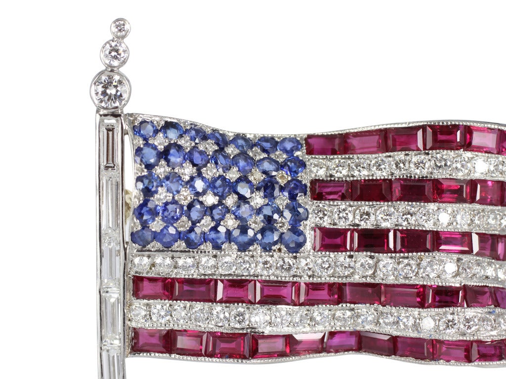 18 karat white gold American flag pin with yellow gold backing consisting of custom step cut rubies, full cut sapphires and round brilliant cut diamonds.