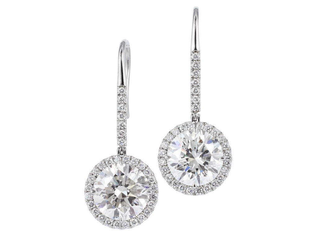 Platinum custom made halo style drop earrings consisting of  one round brilliant cut diamond weighing 7.00 carats, measuring 11.92 - 12.10 x 7.72 mm, having a color and clarity of J/SI2 and GIA Report # 2105794201 and 1 round brilliant cut diamond,