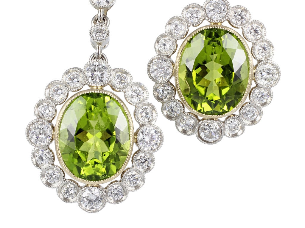 Platinum and 18 karat yellow gold vintage style drop earrings consisting of 2 oval shaped peridot having a total weight of approximately 8.00 carats, the center stones are surrounded by 1 row of full cut diamonds having a total weight of 1.80 carats.