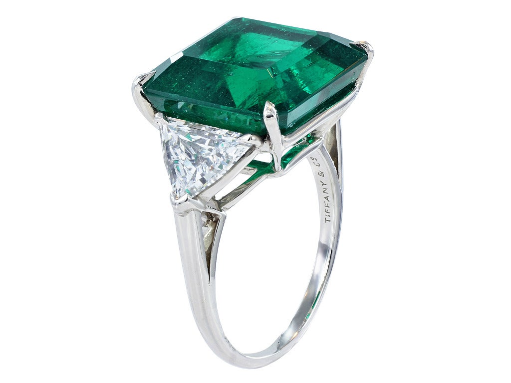 Platinum 3 stone ring consisting of 1 square cut Colombian emerald weighing 11.42 carats, measuring 13.69 x 13.56 x 8.09 mm with Gublin certificate #12110312, the center stone is set with 2 brilliant cut trilliant diamonds and the mounting is signed