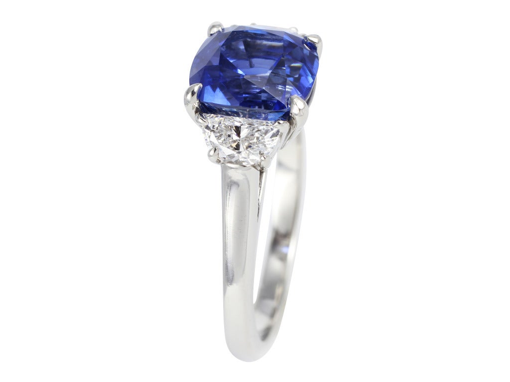 Platinum three stone ring consisting of 1 Burma cushion cut gem blue sapphire weighing 4.18 carats, measuring 8.48 x 8.06 x 6.55 mm with AGL report number CS 54262 stating no evidence of heat and Provenance Burma flanked by 2 half moon diamonds