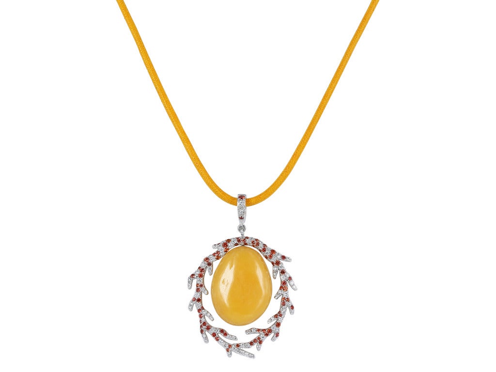 Platinum pendant consisting of 1 oval shaped melo pearl weighing 25.52 carats set with .64 carats total weight of colorless and orange diamonds, the pendant hangs from an orange cord with 18 karat white gold clasp.