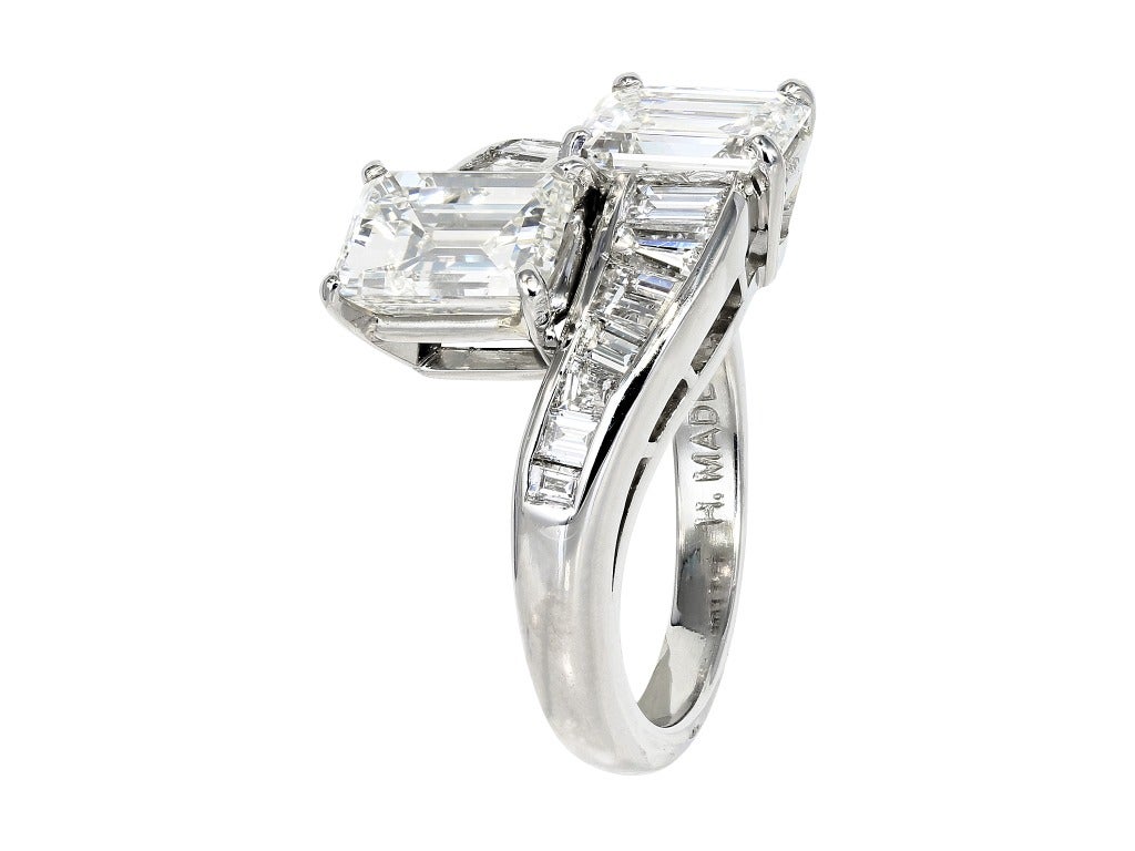Platinum estate bypass ring consisting of 1
emerald cut diamond weighing 1.59 carats and 1
emerald cut diamond weighing 1.18 carats, the 2
stones are set with approximately 1.00 carats total
weight of custom cut baguette diamonds.