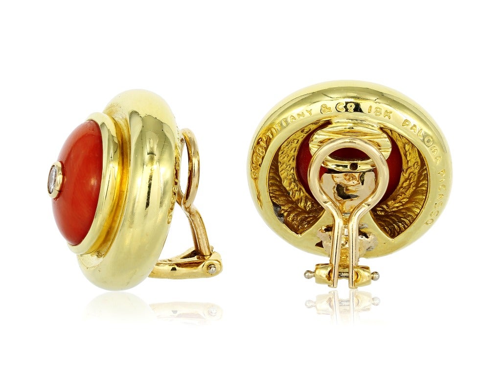 Estate Paloma Picasso for Tiffany & Co, 18 karat
yellow gold button style earrings, consisting of a
wide bezel border set with 2 carved cabochon
corals with a single full cut diamond set flush in the
center of each coral, having an estimated