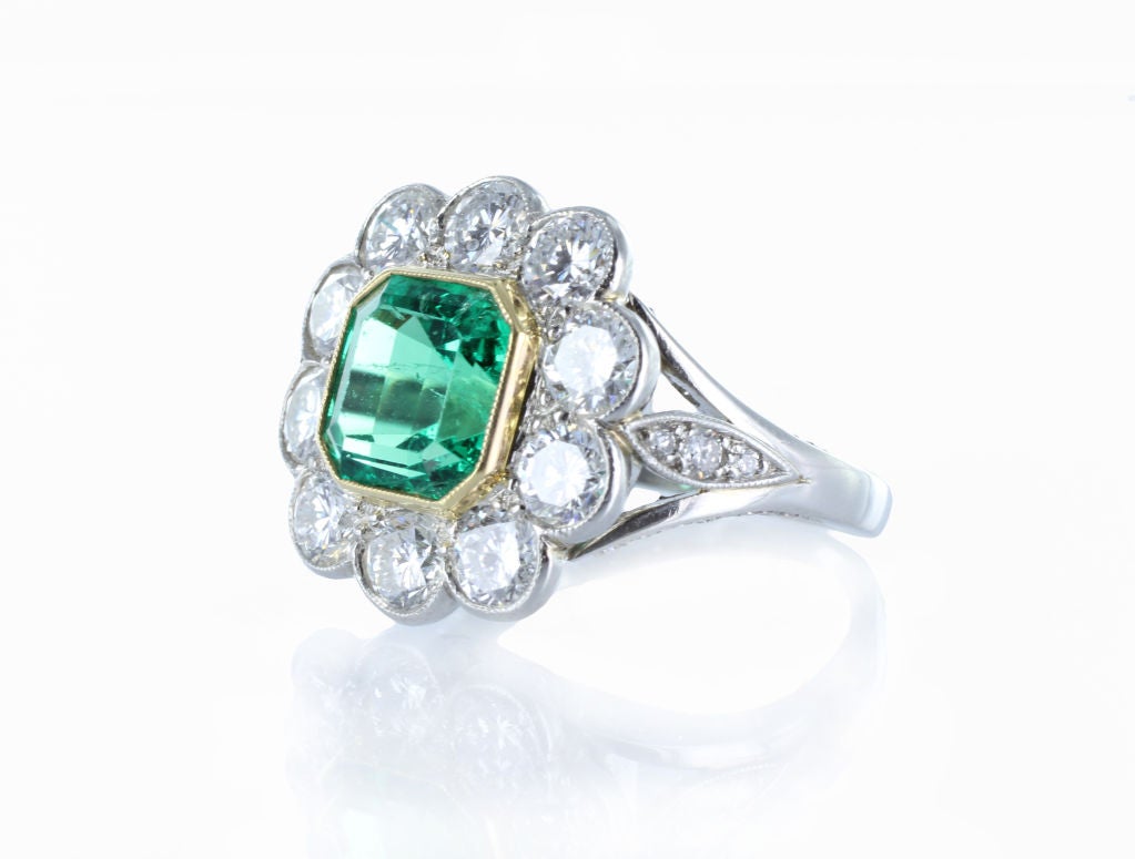 This elegant cluster ring is a beautiful and elegant statement piece. The ring is designed in  platinum and 18 karat yellow gold. The piece features 1 square cut emerald weighing approximately 1.95 carats. The center stone is surrounded by 10 round