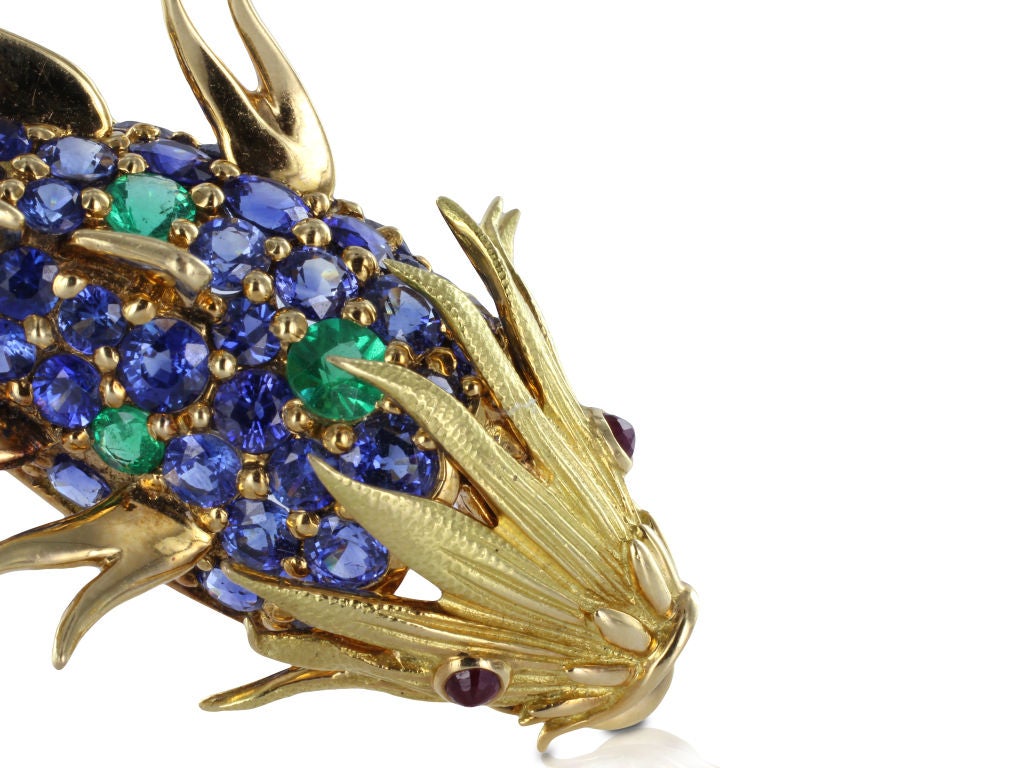 This Vintage 18 karat yellow gold fish pin is an excellent example of the elegance and charm of Schlumberger's work for Tiffany & Co. The fish consists of bead set brilliant blue sapphires and vivid green demantoid garnets with cabochon ruby eyes.