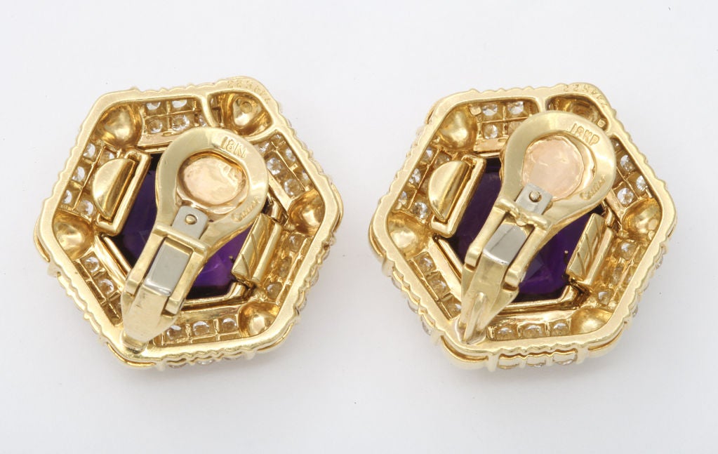 Bold Cartier ear clips of 18K gold with large (and removable) center stones of carved amethyst, complimented by radiating channels of diamonds. Gold and registry marks, and Cartier mark. 1 inch diameter.