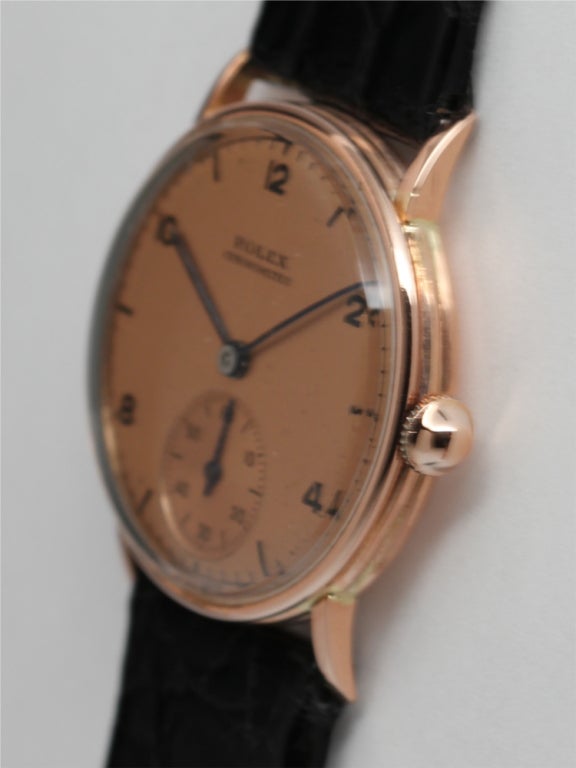 Rolex 14k pink gold mid-size dress model wristwatch, circa 1950s. 26mm diameter case with extended curved lugs. Original antique salmon dial with printed black arabic indexes and baton hands. 17-jewel manual-wind movement with subsidiary seconds.