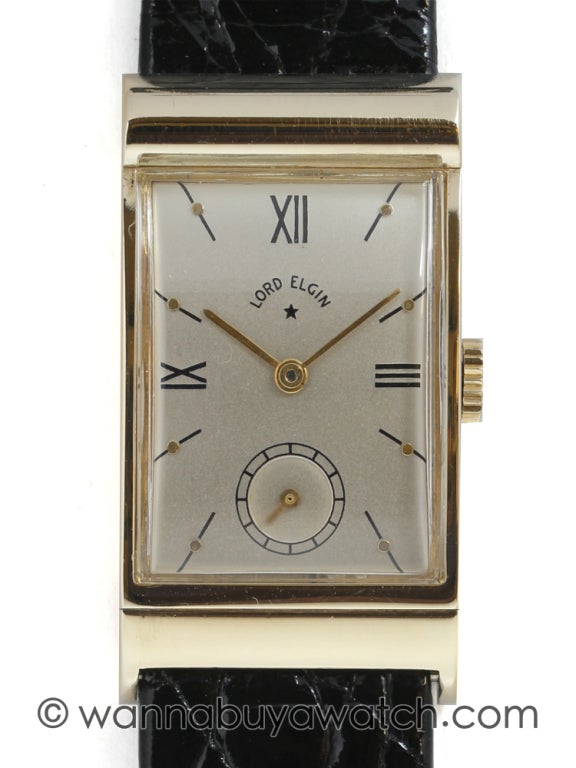 Lord Elgin 14k yellow gold curved rectangular asymmetrical wristwatch 20mm wide X 36mm long, circa 1947. Great looking high-style model contouring scroll design which better faces the wearer. Beautifully restored silvered satin dial with black