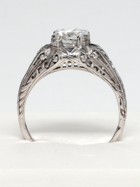 Platinum Art Deco design ring. Featuring a 0.89 carat Old European Cut diamond center stone, rare "E" color and SI2 clarity. Accented by 4 triangular sapphires and 4 diamond side stones. Lovely pierced, scrolled gallery and hand engraved