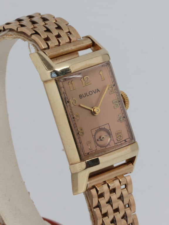 Bulova 14k yellow gold rectangular dress model wristwatch with faceted bezel, circa late 1940's. Salmon dial with raised indexes. 17-jewel manual-wind movement with subsidiary seconds. On a great looking vintage period gilt metal stretch bracelet.