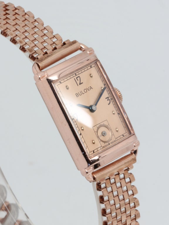 Bulova rose gilt rectangular wristwatch, circa 1940s, salmon-colored dial with raised dots, printed numbers and blued steel hands. 17-jewel manual-wind movement with subsidiary seconds. With period new-old-stock pink gilt combination brick link and