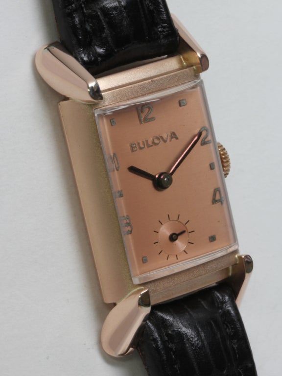 Bulova rose gold-filled rectangular wristwatch with flared lugs, circa 1940s. A very pleasing salmon dial with raised Arabic numerals and blued steel hands. 17-jewel manual-wind movement with subsidiary seconds. Offered on your choice of exotic or