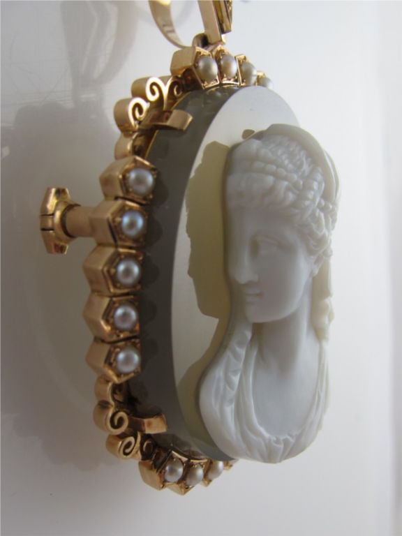 Large & ornate oval Victorian hardstone cameo of a woman with intricately carved hair being held by a scarf & pearls glancing over her right shoulder. White cameo over translucent hardstone in a grey/beige color which becomes almosT clear when held