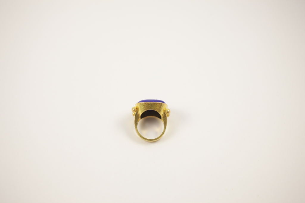 The 19k Elizabeth Locke ring is cushion shaped piece of Lazuli that bears a bee Intaglio. The ring has a split shank and is set in a bezel.