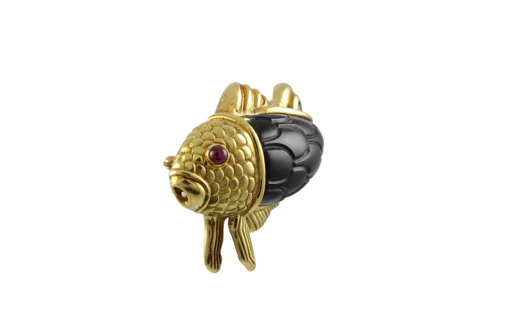 Hammerman and Bros. 18k Yellow Fish Brooch. The body of the fish is carved onyx te resemble scales. The eye is a cabochon ruby and the tail is encrusted with a cabochon emerald.There is a fine liner underneath and a pin stem and a catch.