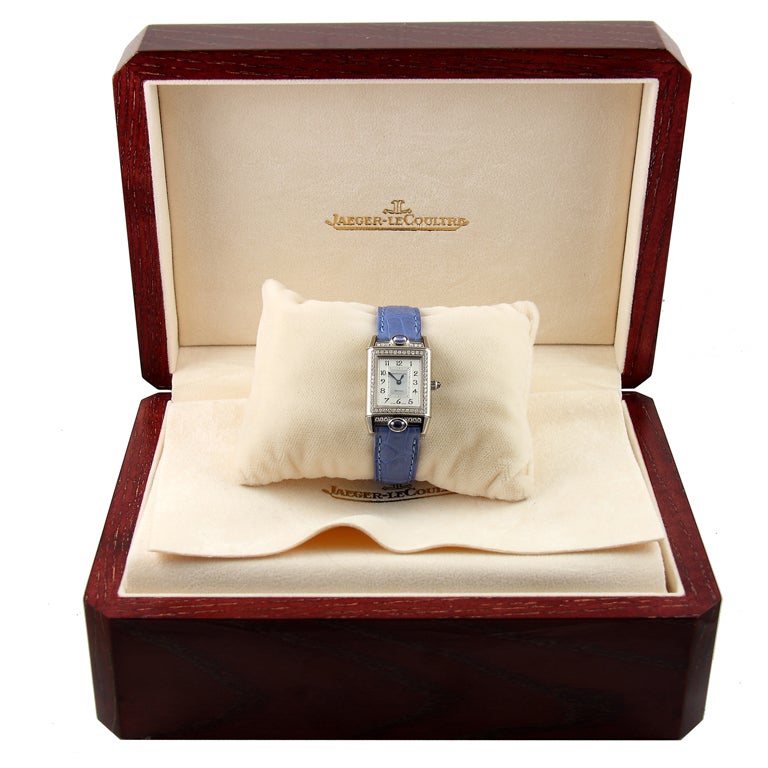 One 18k white gold Jeager-LeCoultre Reverso wristwatch. The strap is light blue ostrich with an 18k white gold deployment buckle. The face is white with a diamond bezel. Two blue cabochon sapphires are on the edge of the case. Numbered 2015466.