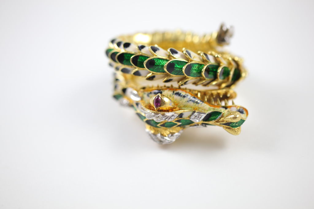 18kt yellow gold flexible dragon spiral cuff bracelet. Body is enameled in green, white and black and the eyes are each set with on marquis ruby (.50ctw). Pave diamonds accent the head and the body with 37 in total (.55ctw). The segmented sections