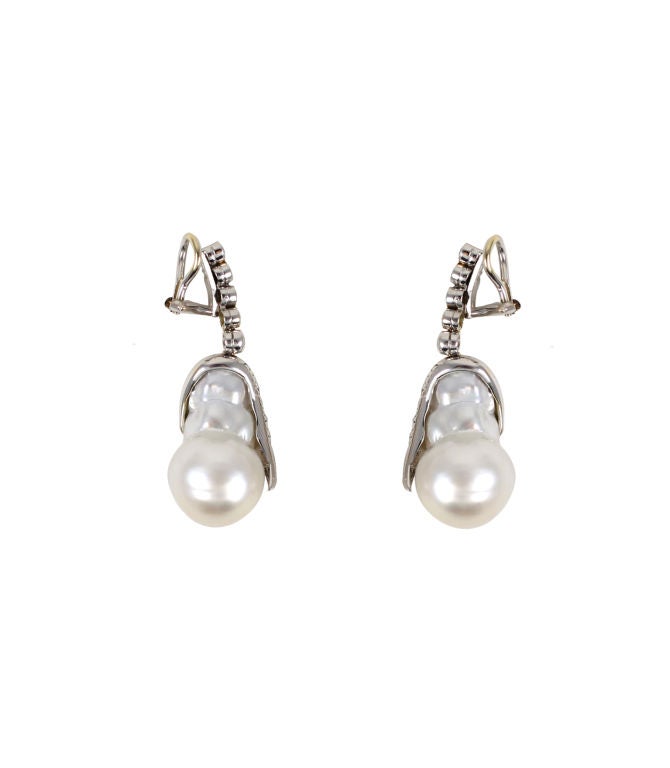 Pair of 18k white gold clip-back earrings set with diamonds and one baroque pearl each. The top portion is bezel-set with five round brilliant diamonds and the bottom half is bead-set with nine round brilliant diamonds; estimated total diamond