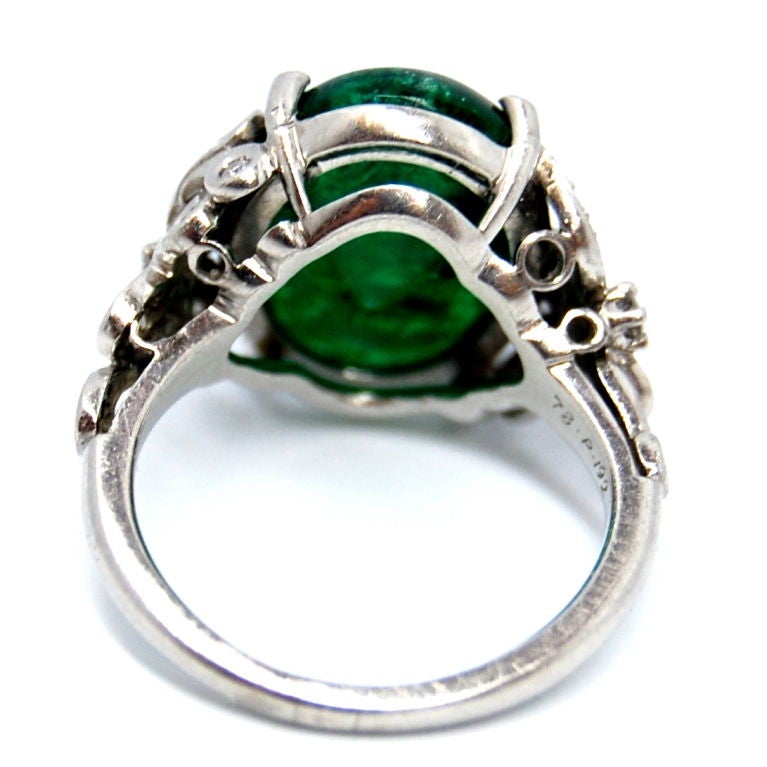 An exquisite emerald cabochon green gemstone in a scrolled platinum setting, accompanied by diamonds.
