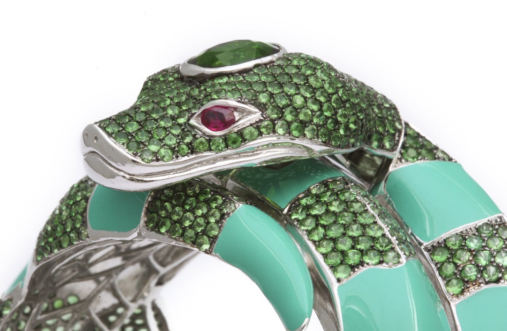 This snake bracelet features green enamel and a mixture of green tourmaline and tsavorite garnet, expertly set in silver.  The eyes are oval rubies and the head is set with an oval chrome tourmaline.  The unique clasp mechanism is a testament to the