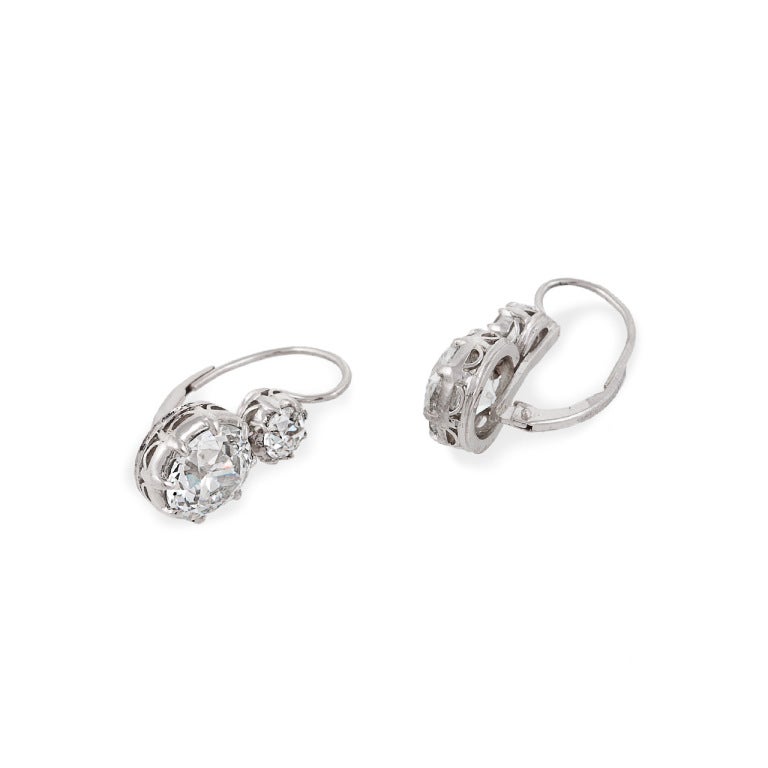 One pair of platinum and diamond 2-stone earrings, contemporary mountings, diamonds circa 1925. One earring centers 1 transitional round brilliant diamond, 3.30 carats, color: K, clarity: VS2, one earring centers 1 old European-cut diamond, 3.09