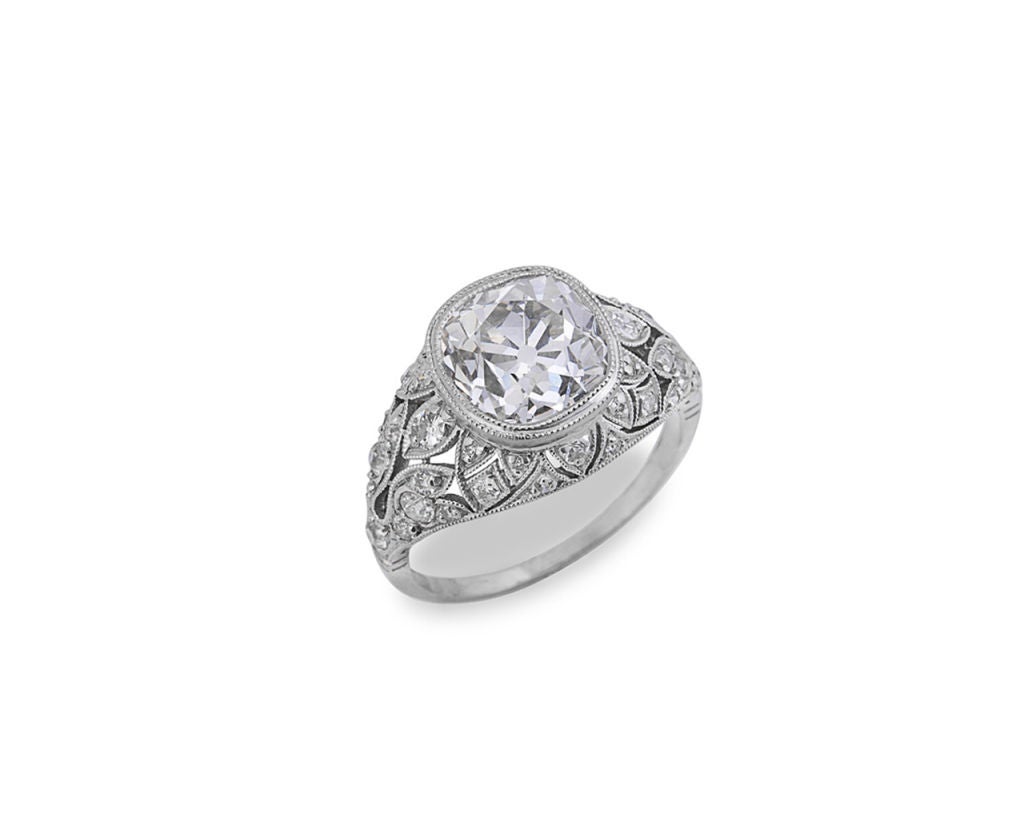 The ring centers 1 bezel-set cushion-cut diamond in a pierced, diamond-set mounting. All settings have millegrain edging. Center diamond weighs 3.40 carats, color: H, clarity: VS1 and is accompanied by a European Gemological Laboratory Certficate,