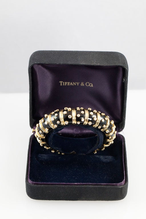 The bracelet alternates bands of yellow gold and black paillonne enamel decorated with raised, bezel-set round brilliant-cut diamonds. The bracelet is signed 