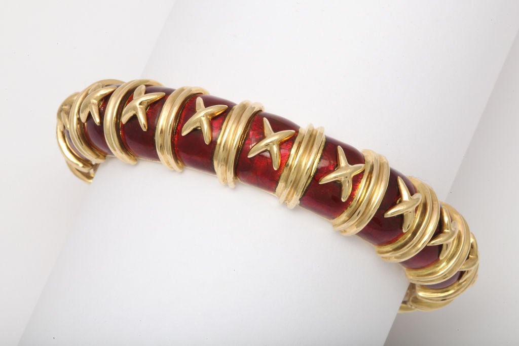 An enamel and gold bracelet, by Jean Schlumberger, Tiffany & Co. Designed as a red pailloné enamel hinged bangle, decorated with sculpted 18k gold vertical bands and cross motif detail, mounted in gold.